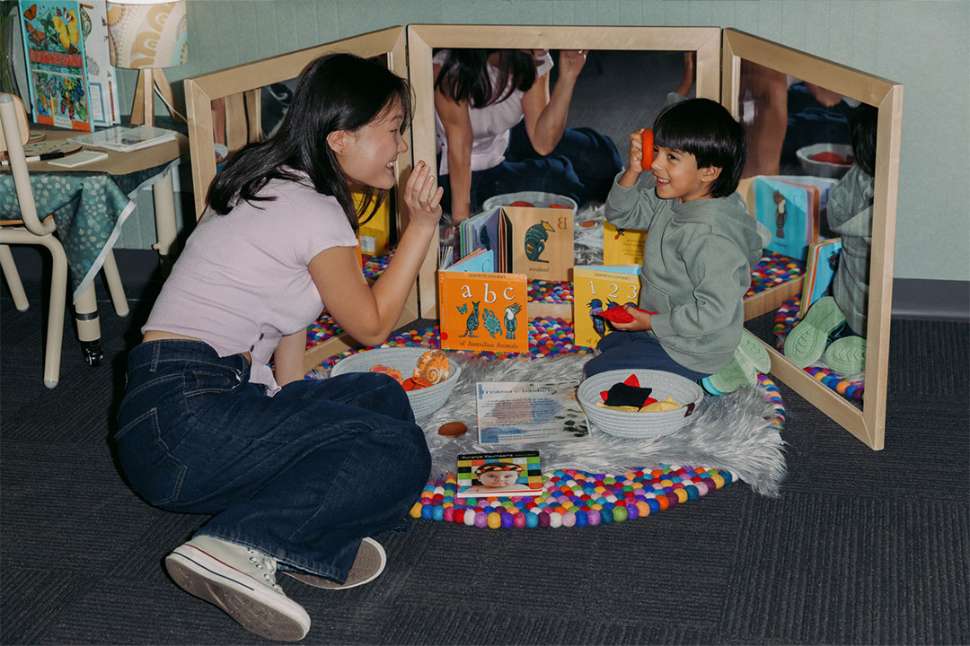 A early education teacher interacting with a student with a book.