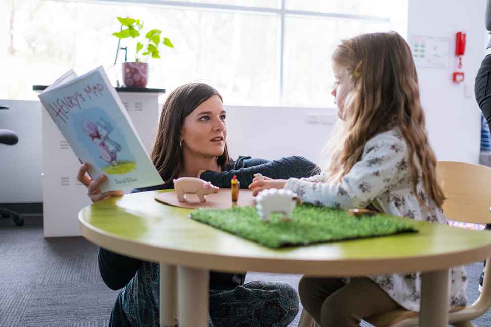A early education teacher interacting with a student with a book.