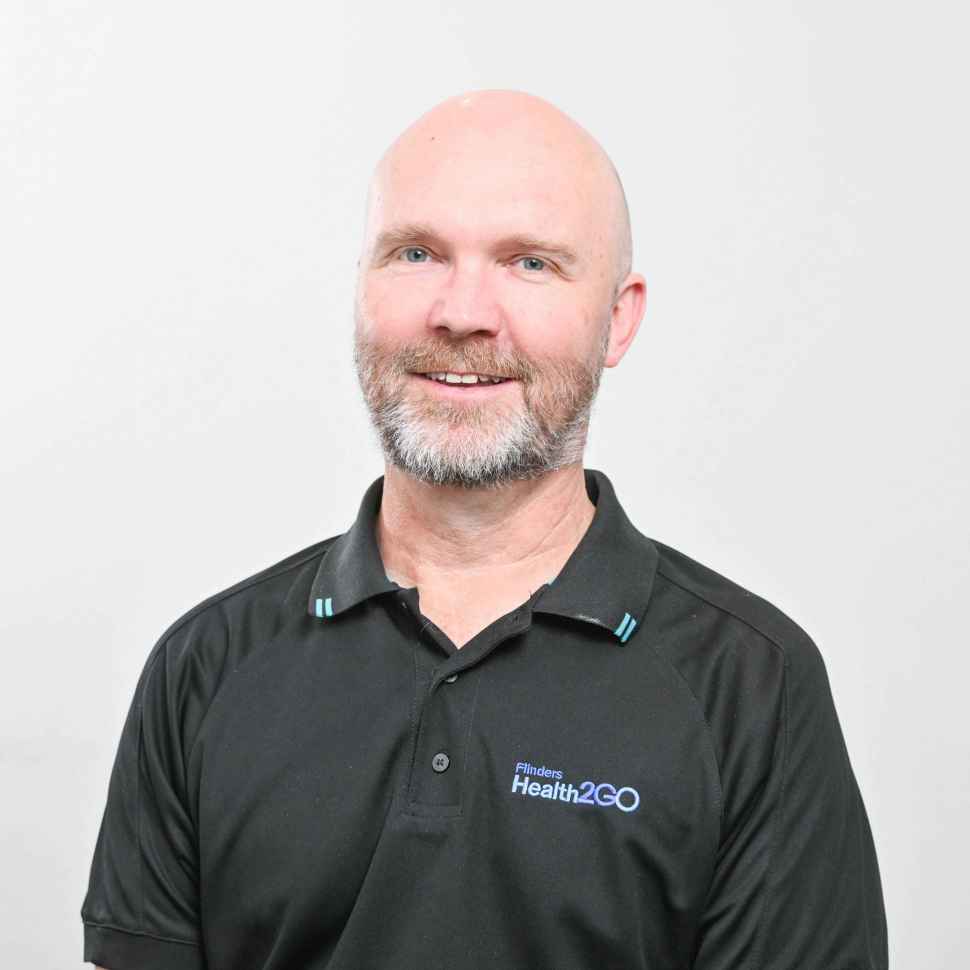A man wearing a black polo behind a white backdrop