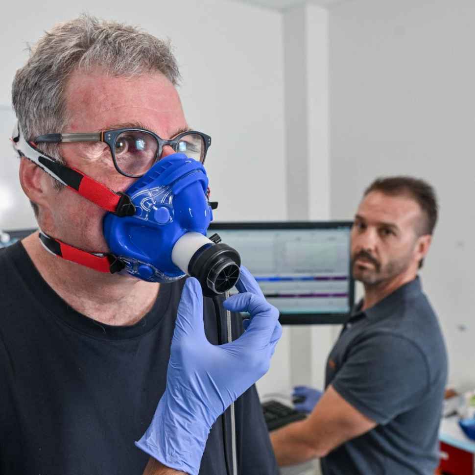 Man with mask on for exercise testing with clinician stood behind him
