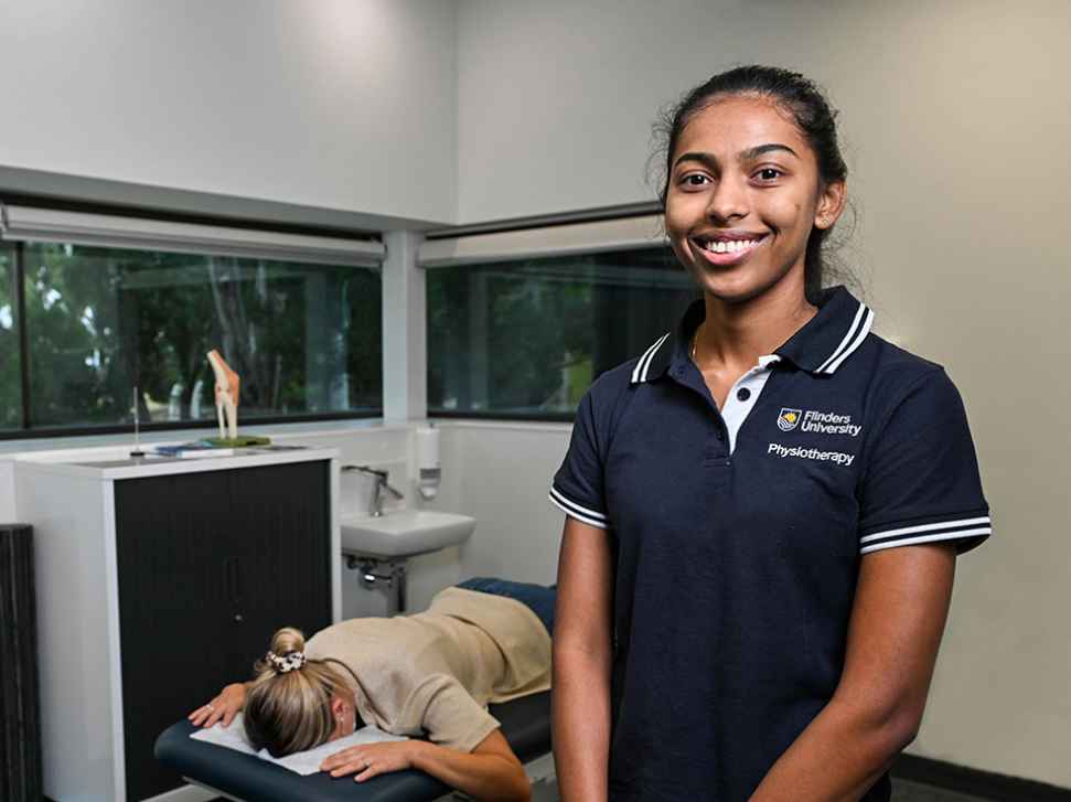 Flinders Physiotherapy Student smiling at camera with patient lying on bed in background