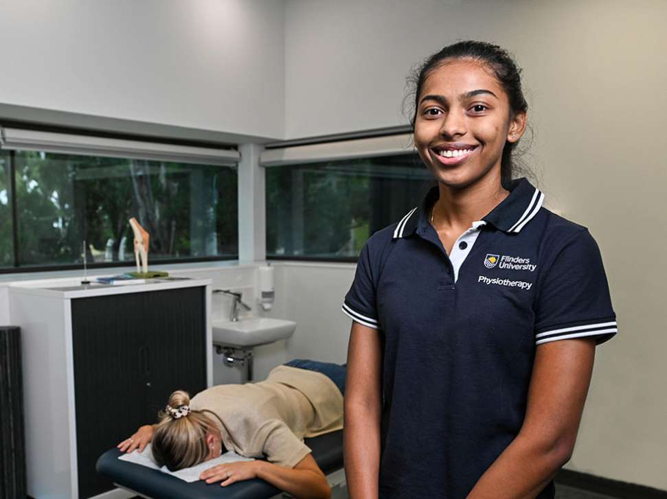 Flinders Physiotherapy Student smiling at camera with patient lying on bed in background