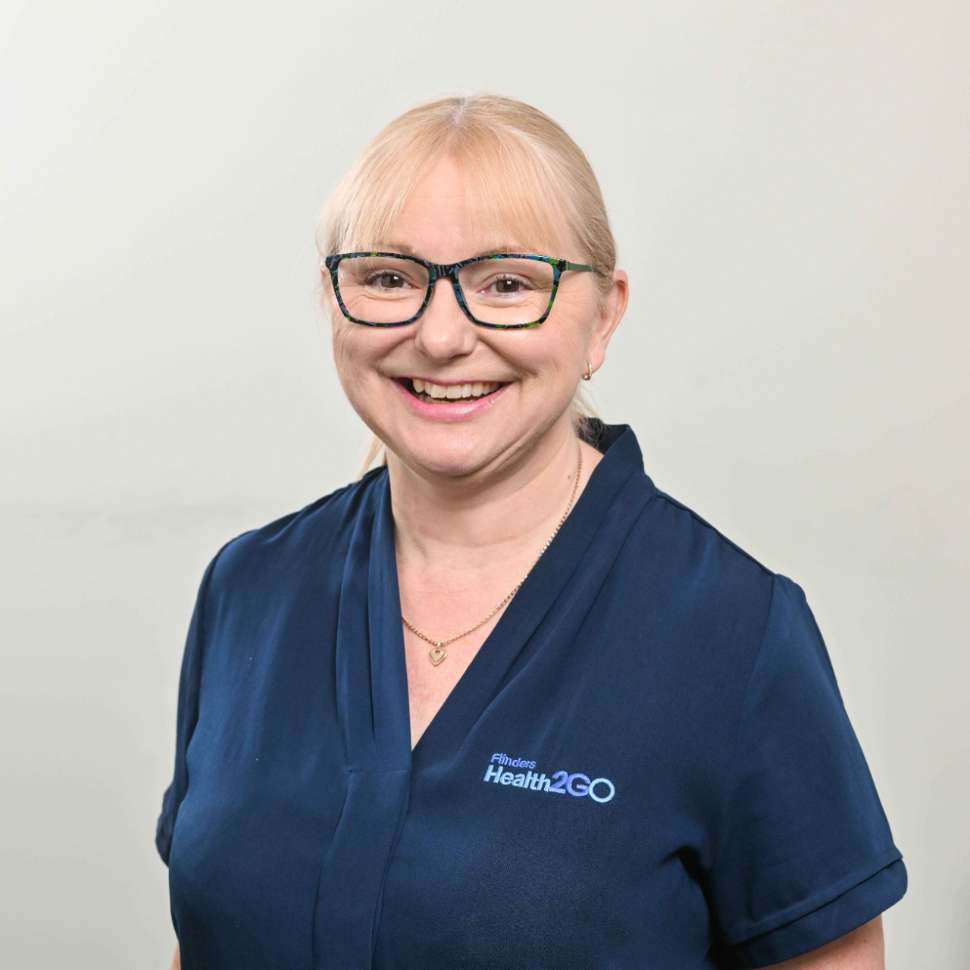 A woman wearing a navy top and glasses behind a white backdrop