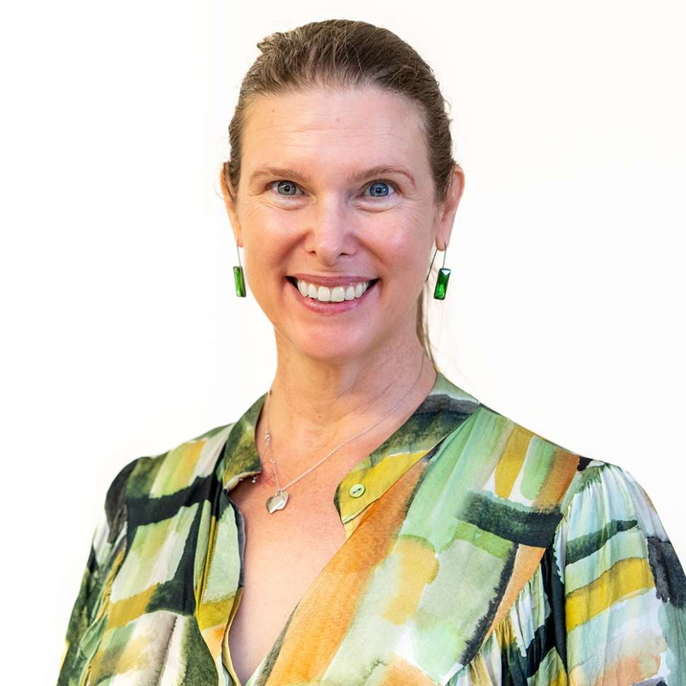 Smiling woman in a multicoloured shirt behind a white backdrop