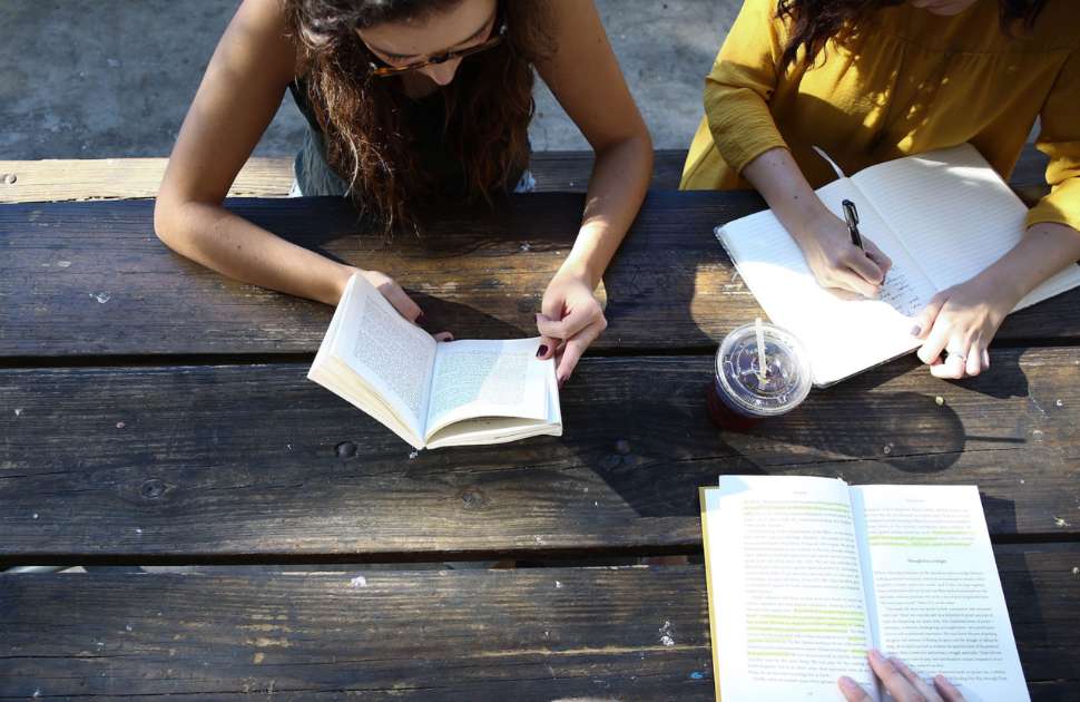 Image of students on an outdoor bench reading and writing